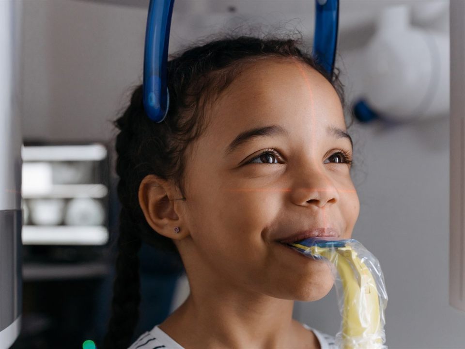 Smiling girl holding a digital X-ray sensor in her mouth at our pediatric dentist office in Christiansburg, VA